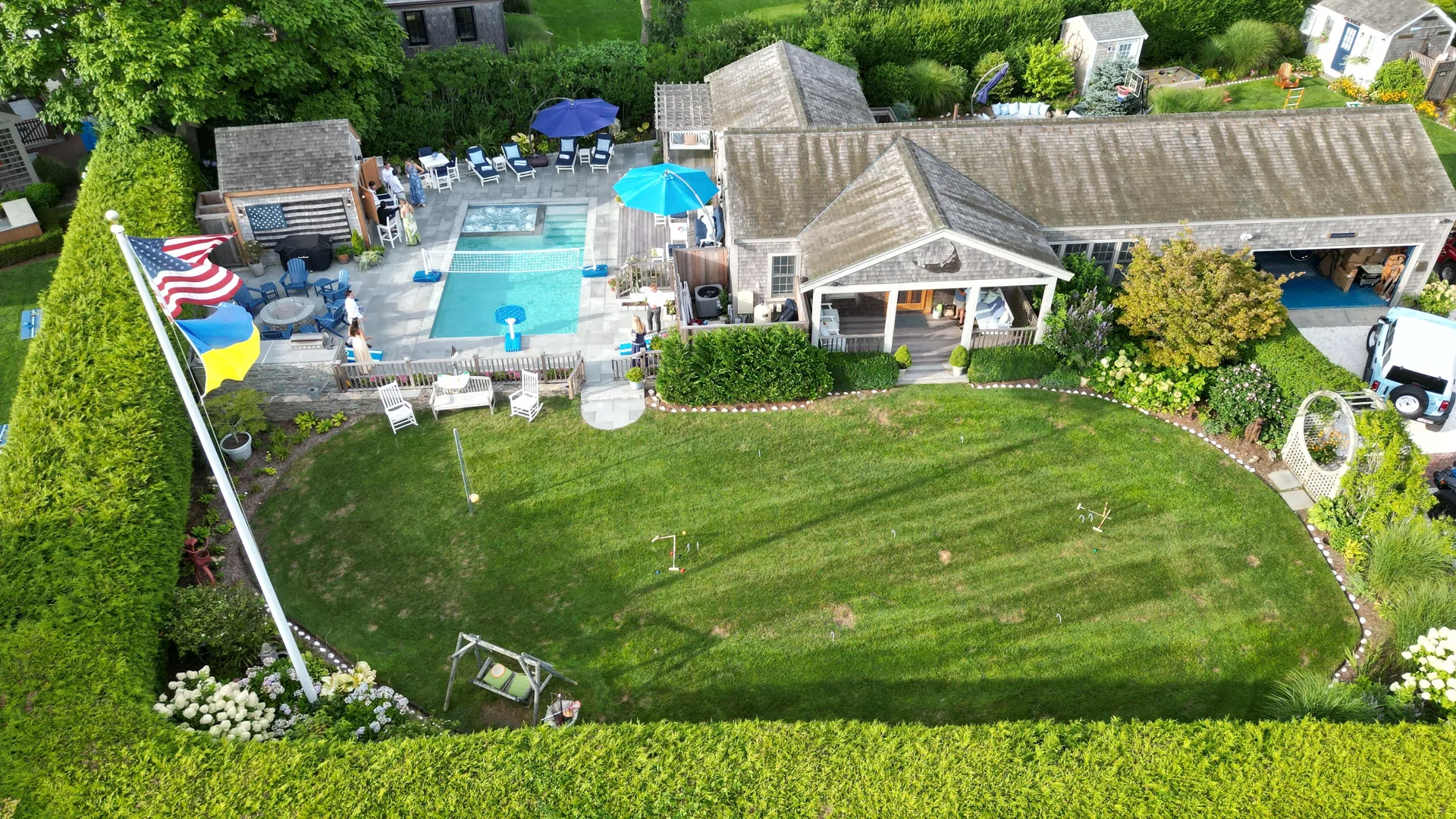 The Mini Compound from above: the pool and spa with its volleyball net, the cabana and outdoor kitchen, US and nautical signal flags flying on the pole, and a broad croquet lawn running out from the porch under the whale nameboard.