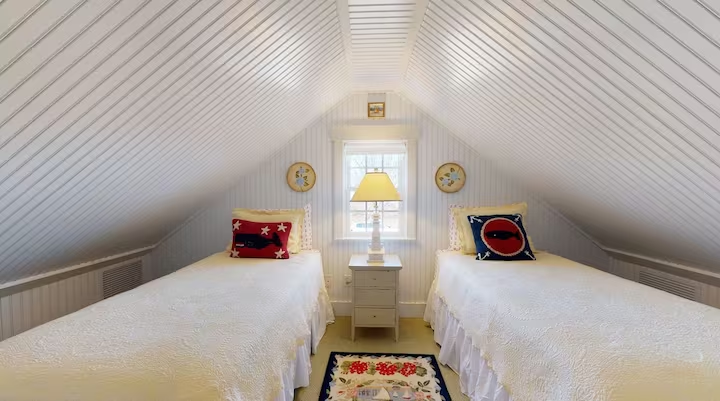 Twin beds set under the sloping ceiling of an attic room.
