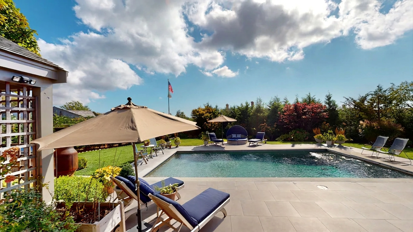 The private heated pool with navy loungers, tan umbrellas, a canopied daybed, and a bluestone surround backed by lawn and gardens